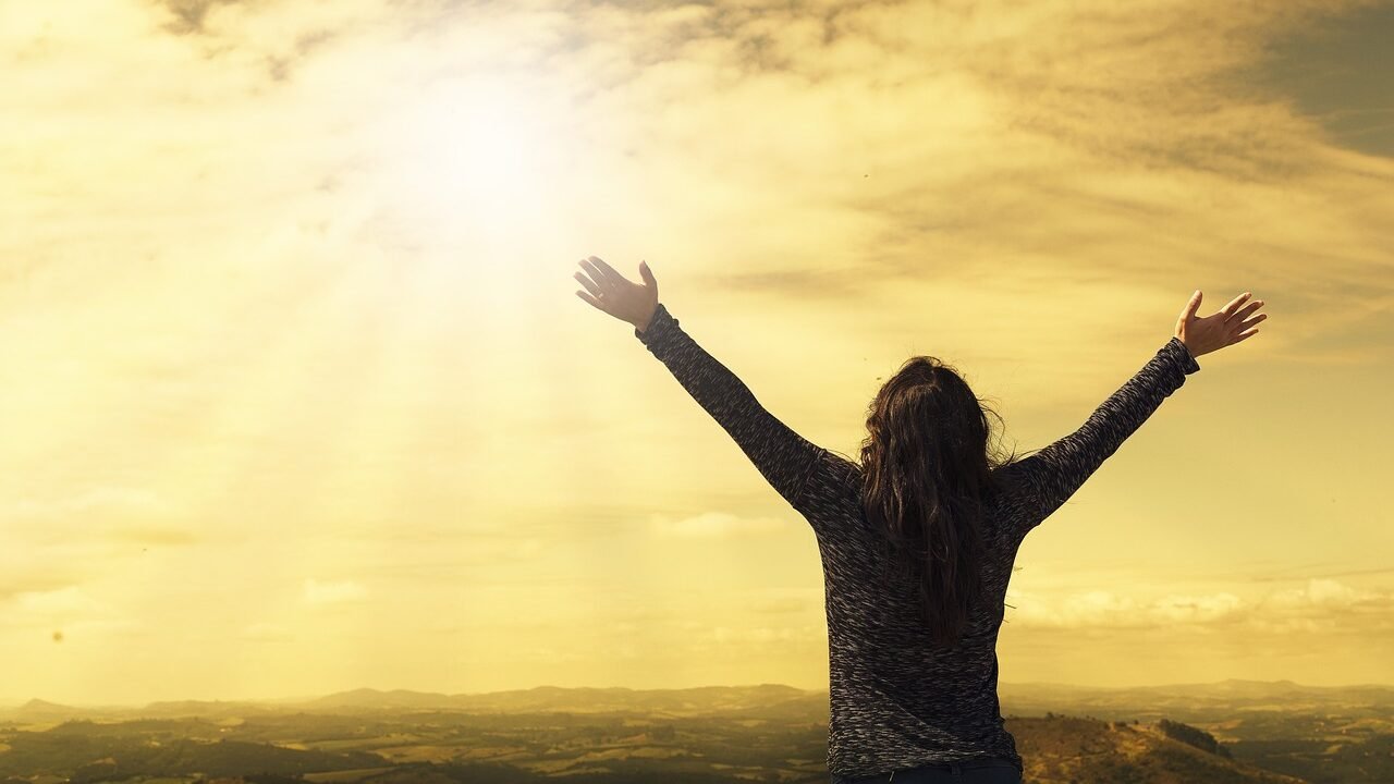 Woman standing with arms open wide toward the sunlight, listening and worshiping.